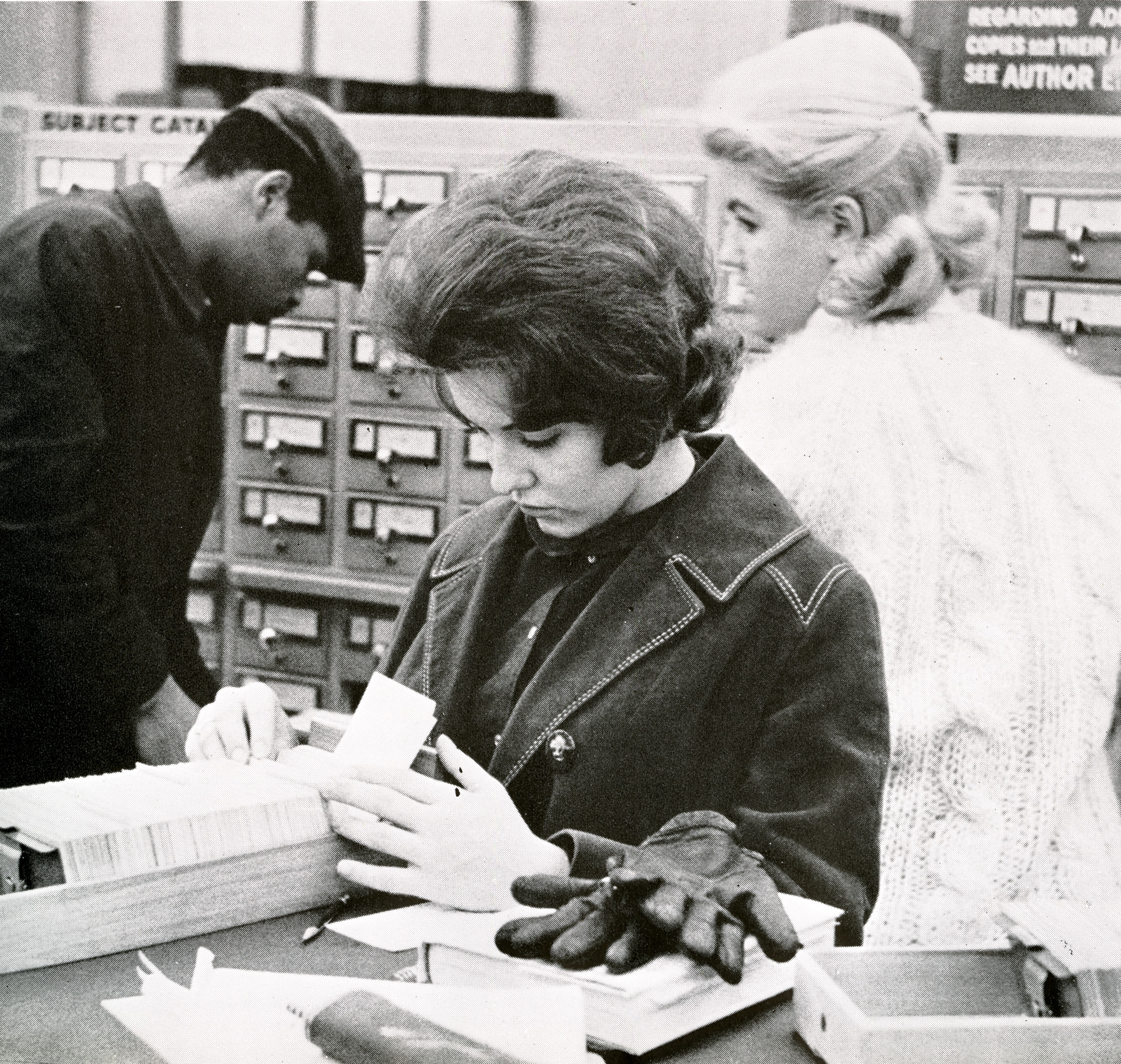 Three students access catalogue cards in the library, circa 1964