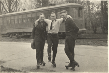 Three students roller skate next to a streetcar, circa 1922