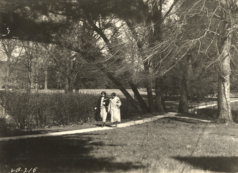 Two students walk on campus, ca. 1920