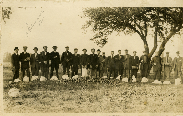 Students standing next to a pile of apples, 1912