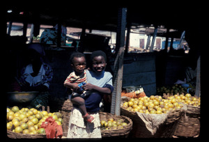 Girl, 10-12 years old, holding infant before orange stalls