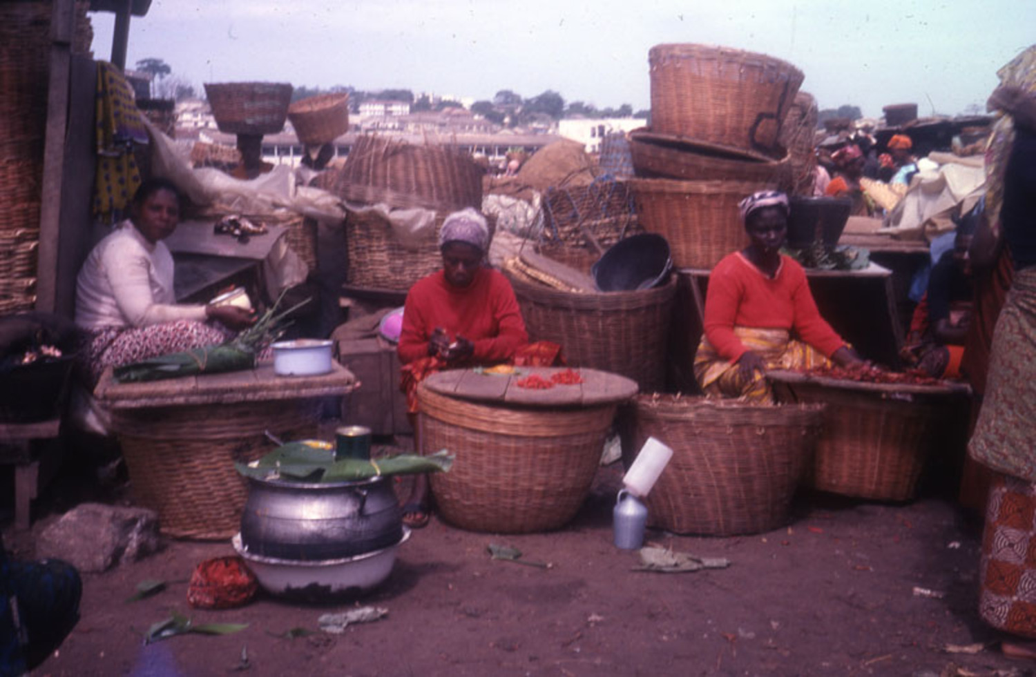 Three seated women with baskets and trays of dried pepper