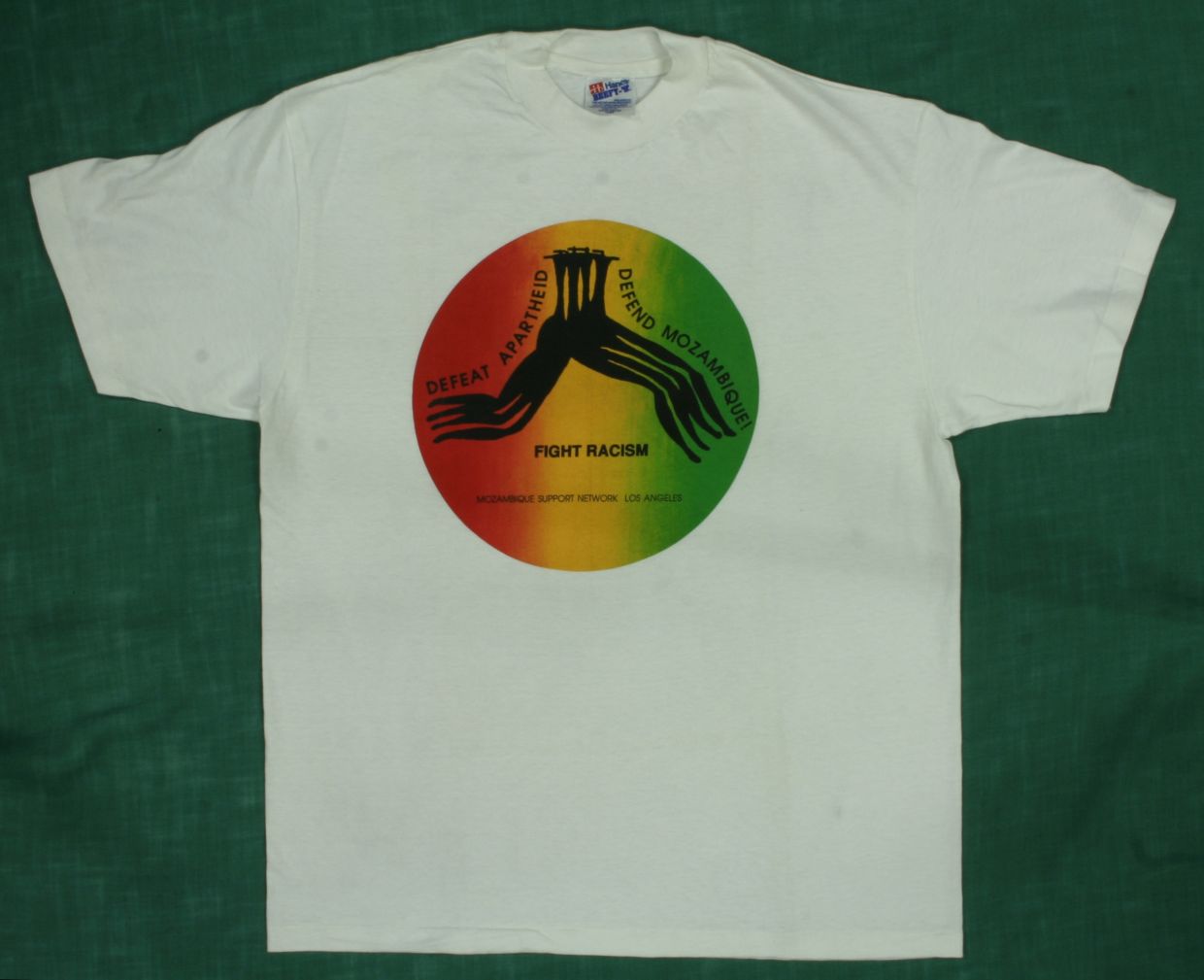 The T-shirt design, by Rachel Chapman, shows four black, abstract figures leaping together across a circle with a horizontal pattern of red, yellow, and green. The T-shirt was also produced with a white design on black. The &ldquo;Baobab News&rdquo; December 1992 / January 1993 issue (available on this website) announced that the shirt was available for sale.